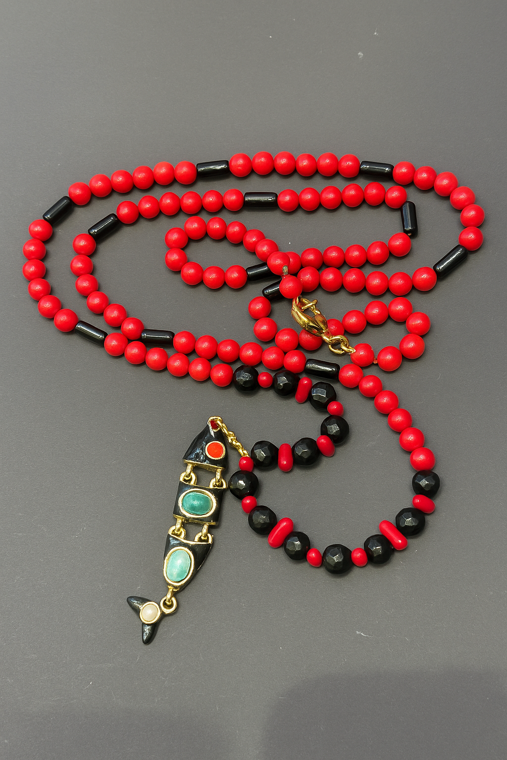 Vivid Tide Necklace | Κολιέ Κοράλλι και Αχάτης | Toucan Concept Store Μακρύ Vivid Tide Necklace (92εκ) από στρογγυλές κόκκινες χάντρες κοραλλιού και μαύρες χάντρες αχάτη, με χρυσά διαχωριστικά και ένα μεγάλο μεταλλικό στοιχείο σε σχήμα ψαριού διακοσμημένο με πολύχρωμες πέτρες.